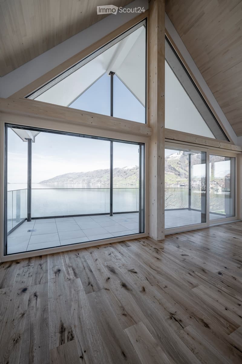 Bright, airy attic space with wooden floors, large skylights, and expansive windows overlooking a lake and mountains.