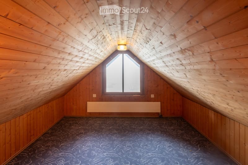 Empty attic room with wooden walls and ceiling, a skylight window, and patterned carpeting.