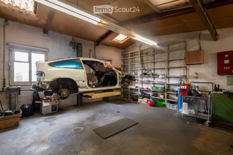 A spacious garage with a partially disassembled car on a workbench, surrounded by shelves filled with tools and equipment, and a variety of storage items.