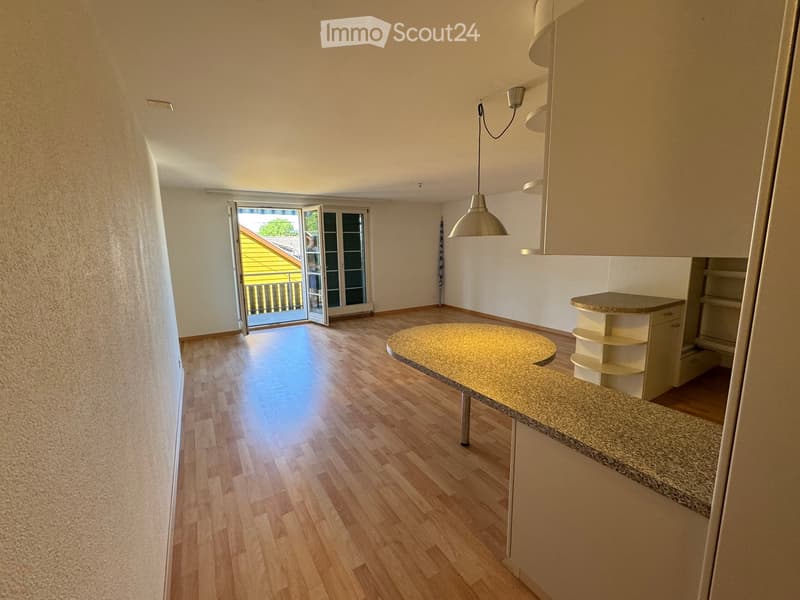 Bright, open room with wooden flooring, a round table, a pendant light, and a cabinet. Large sliding glass doors lead to a balcony.