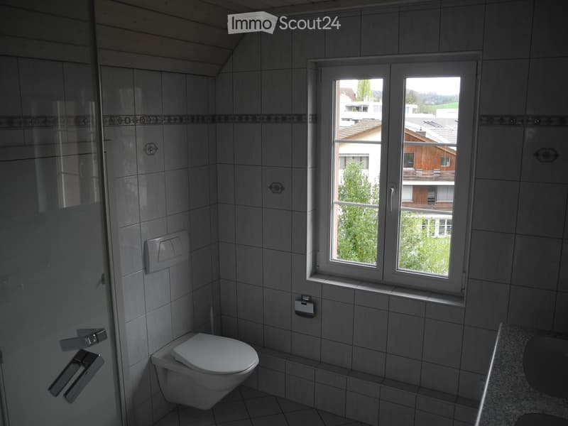 Modern bathroom with grey tiles, a toilet, a sink, and a window offering a view of the surrounding area.
