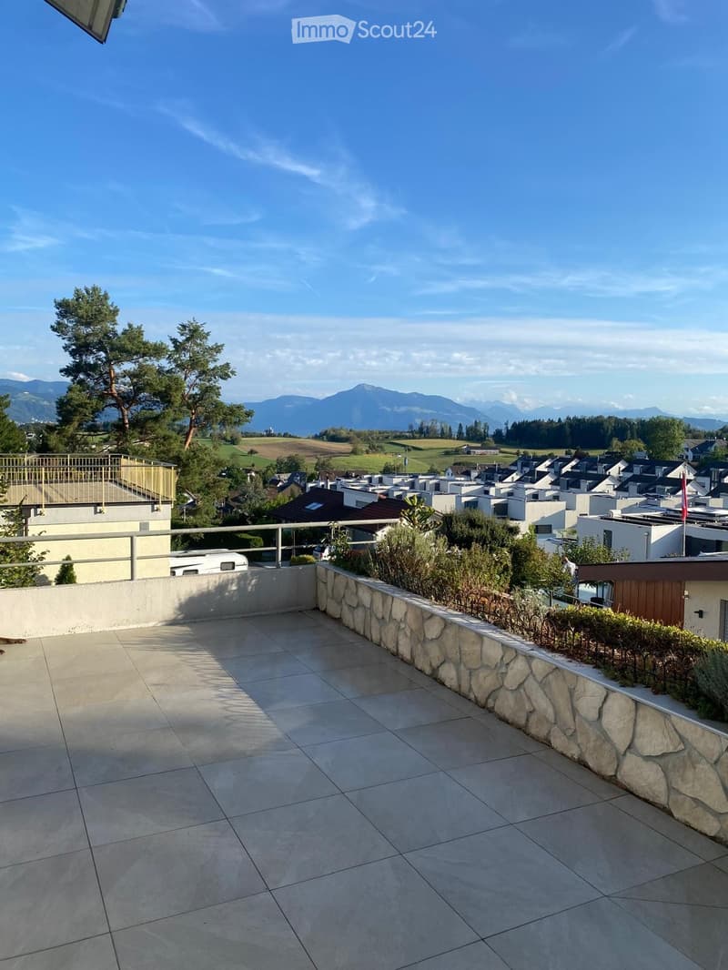 Spacious balcony with tiled floor, stone wall, metal railing, and scenic mountain view.