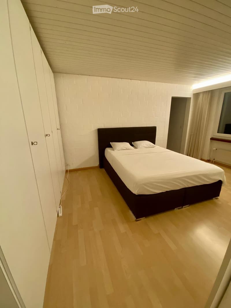 Minimalist bedroom with a single bed, white pillows, light wooden flooring, and white brick walls.