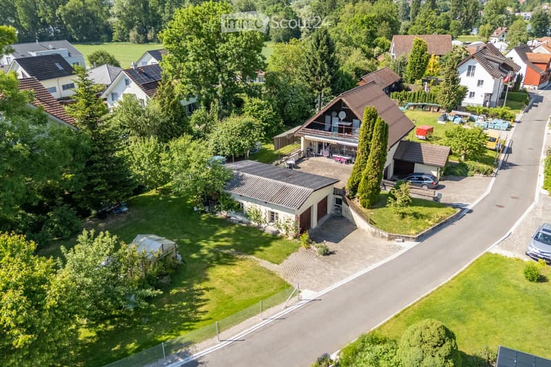 Aerial view of a residential area with multiple houses, gardens, driveways, and parked cars.