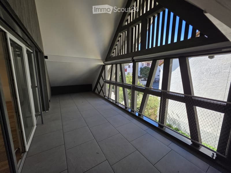 Balcony with tiled floor, metal railing, and large windows offering a view of the surrounding area.