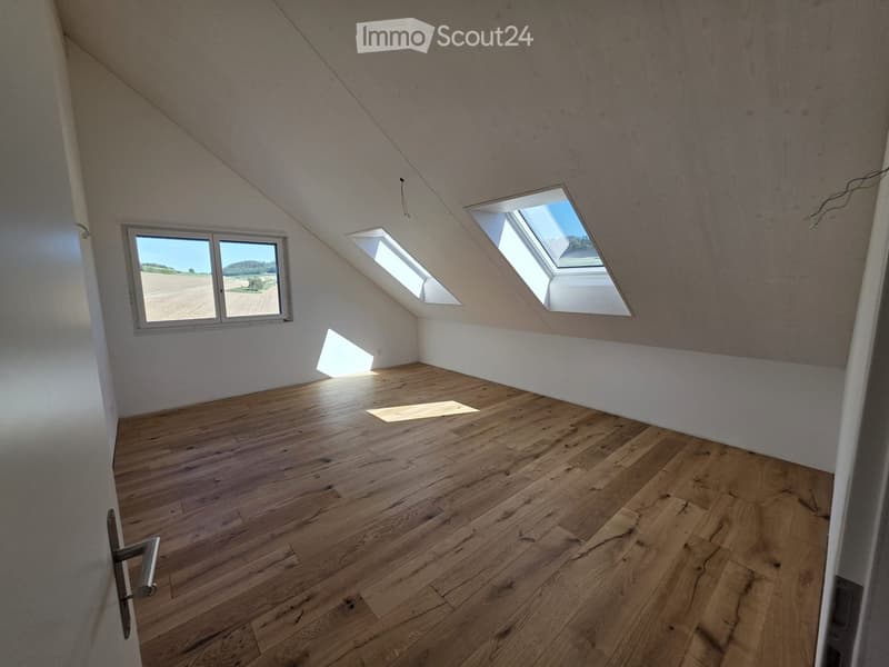 Empty attic room with wooden flooring, white walls, and skylight windows allowing natural light to enter.