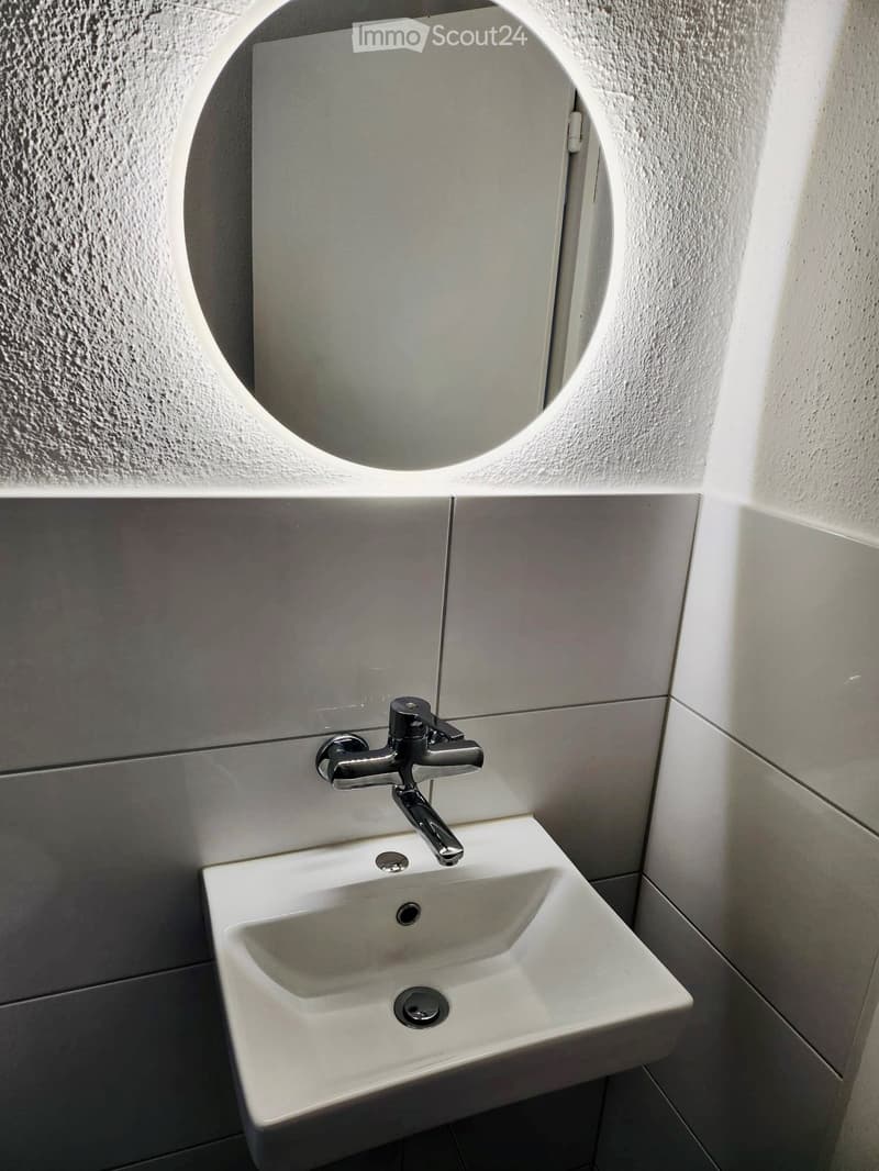 Modern bathroom with a white sink, chrome faucet, and a round mirror above it.