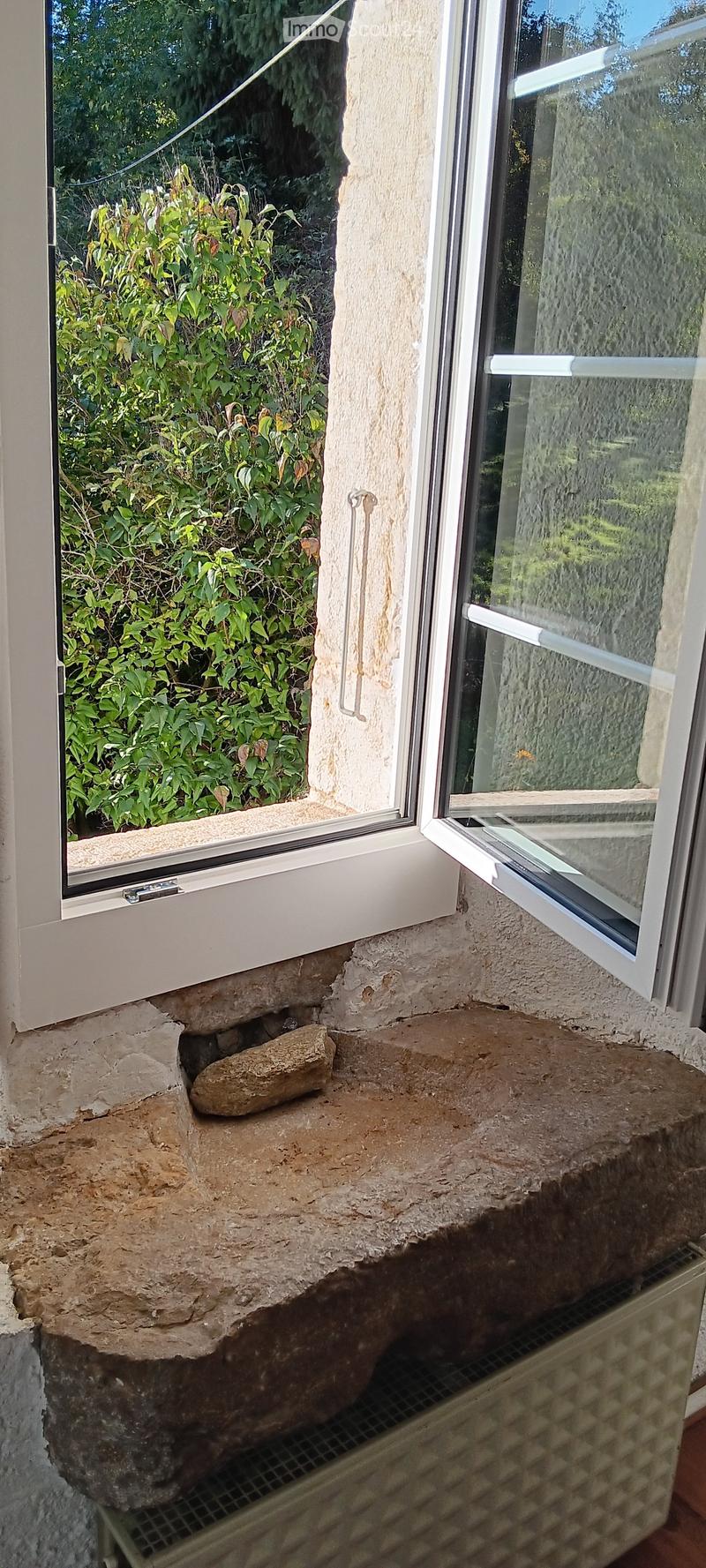 Balcony with stone seating area, large windows, and lush greenery visible outside.