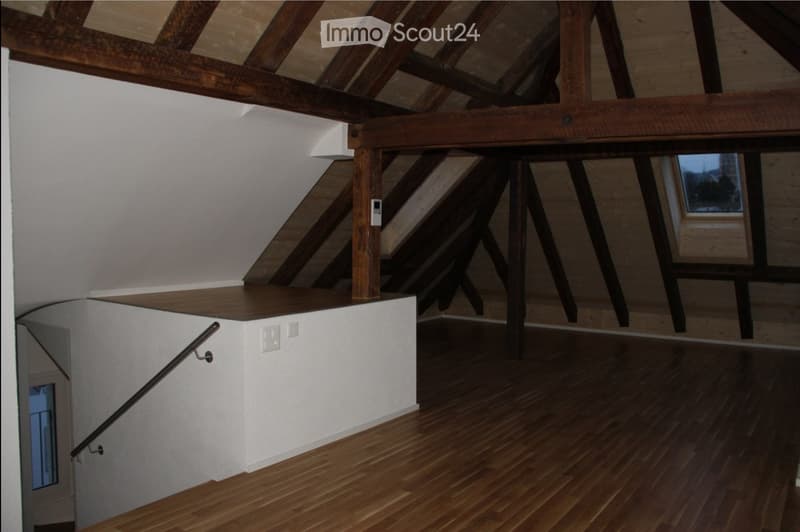 Staircase with wooden steps and handrail, white walls, exposed wooden beams, and a small landing area with built-in storage.
