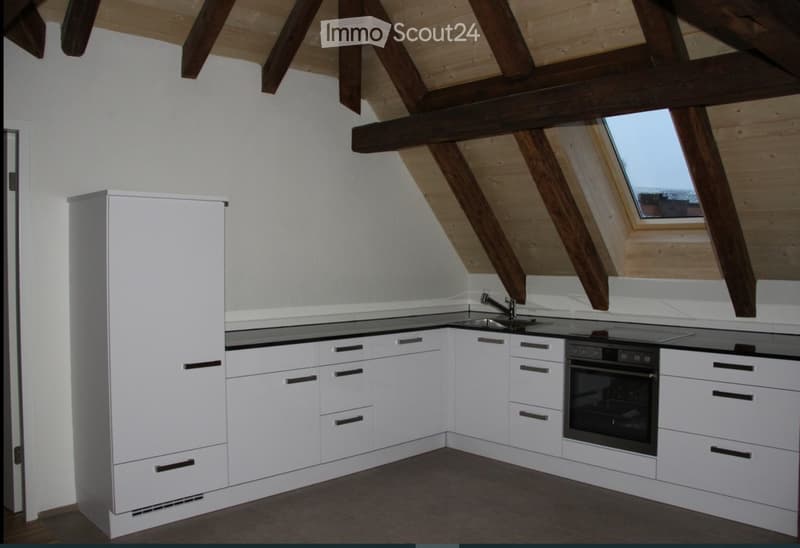 Modern kitchen with white cabinets, stainless steel sink, and built-in oven, featuring exposed wooden beams and skylight windows.