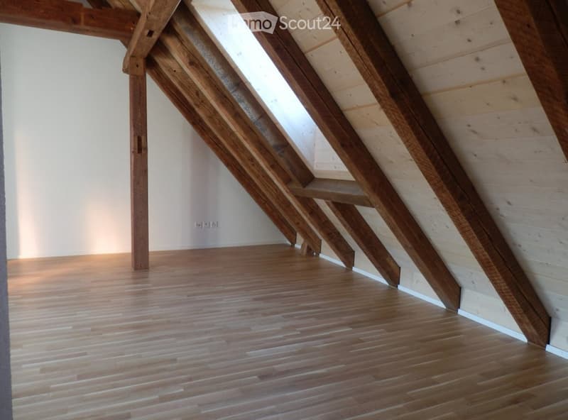 Empty attic space with wooden beams, slanted wooden ceiling, and wooden floor.