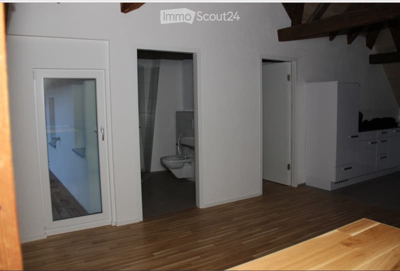 Empty room with wooden flooring, white walls, and three open doors leading to a bathroom, a closet, and another room.