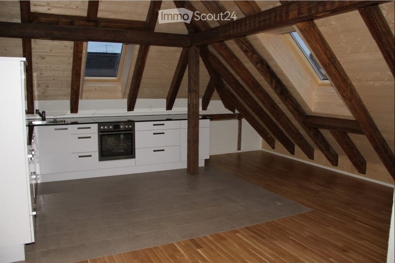 Modern kitchen with white cabinets, stainless steel oven, and a sink. Exposed wooden beams and skylights create a bright, airy space with a mix of tiled and wooden flooring.