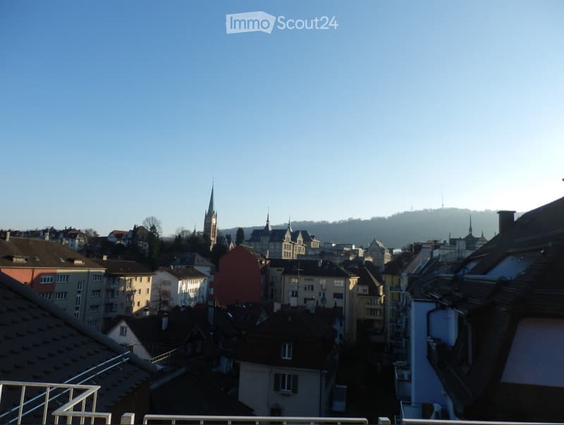 View from a balcony overlooking a cityscape with various buildings, including a prominent church tower, under a clear blue sky.
