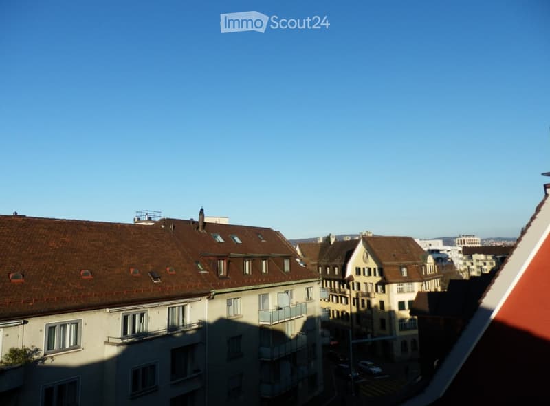 View of a cityscape with multiple residential buildings featuring brown tiled roofs, balconies, and windows, under a clear blue sky.