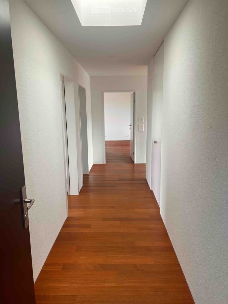 Empty hallway with wooden flooring, white walls, and several doors leading to other rooms.