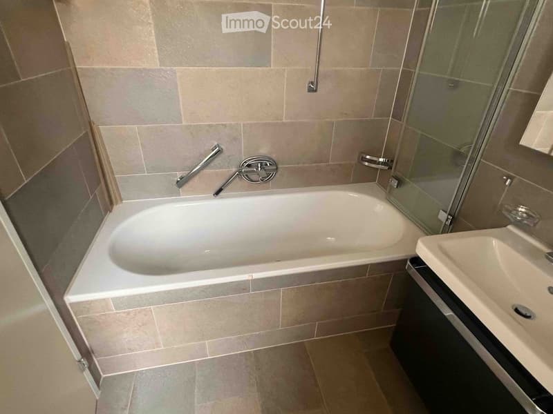 Modern bathroom with a bathtub, sink, and glass shower enclosure. Features beige tiles and chrome fixtures.