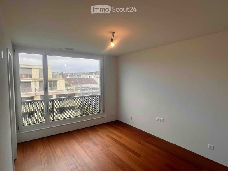Empty room with wooden flooring, large window with balcony access, and visible electrical outlets.