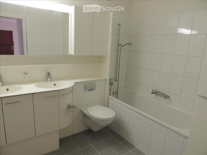 Modern bathroom with white tiles, a double sink vanity, a toilet, a bathtub with a showerhead, and a large mirror above the sink.