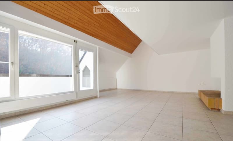 Empty room with white walls, tiled floor, large windows, and a wooden bench in the corner.