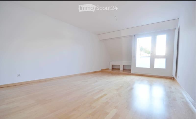 Empty room with wooden flooring, white walls, and large windows with sliding doors leading to a balcony.