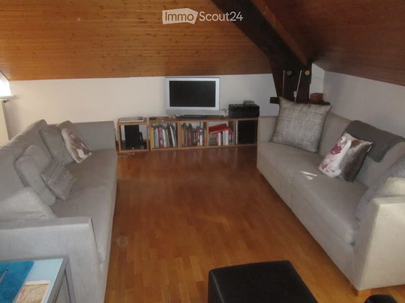 Living room with wooden flooring, two sofas, an ottoman, a television, and a bookcase.