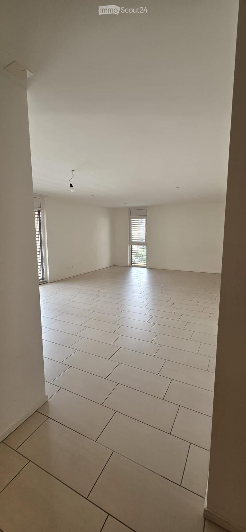 Empty room with white tiled floor and white walls, featuring a single window with blinds and a visible light fixture on the ceiling.