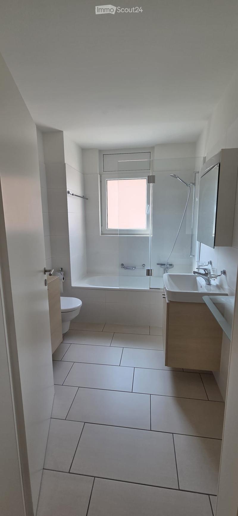 Modern bathroom with white tiles, a bathtub with a glass shower enclosure, a toilet, a double sink with a modern faucet, and a mirrored cabinet.