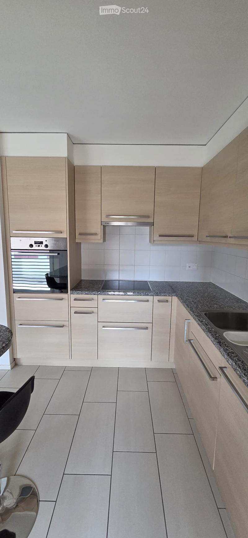 Modern kitchen with light wood cabinets, stainless steel appliances, granite countertops, and tiled flooring.