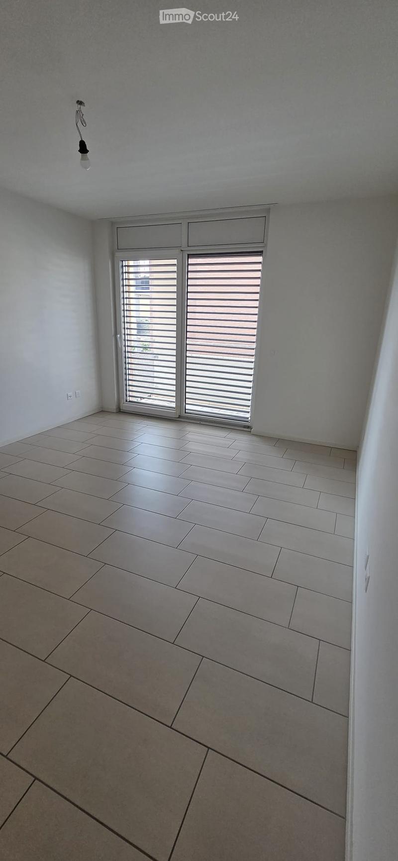 Empty room with tiled floor, white walls, and a large window with blinds. No furniture or equipment is present.