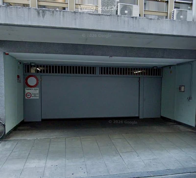 Underground parking area with a large, closed garage door, tiled floor, and security features including a barred window and signage.