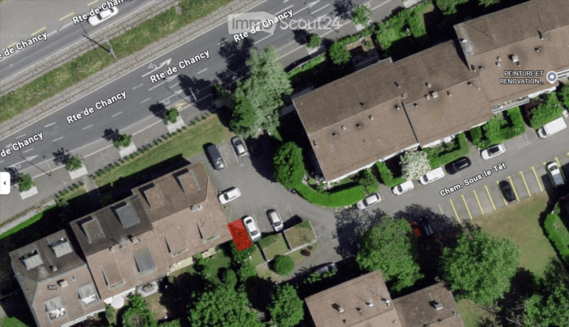 Aerial view of a residential area showing multiple houses with brown tiled roofs, surrounded by trees and parked cars along the street.
