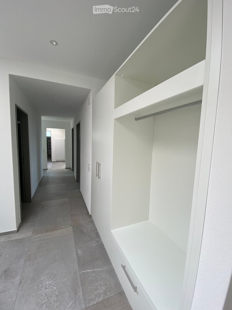 Empty hallway with white walls, gray tiled floor, built-in closet with shelves and drawers, and recessed lighting.