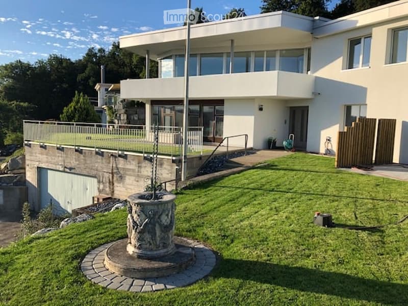 Modern two-story house with white exterior, large windows, raised ground floor, garage, and well-maintained lawn.