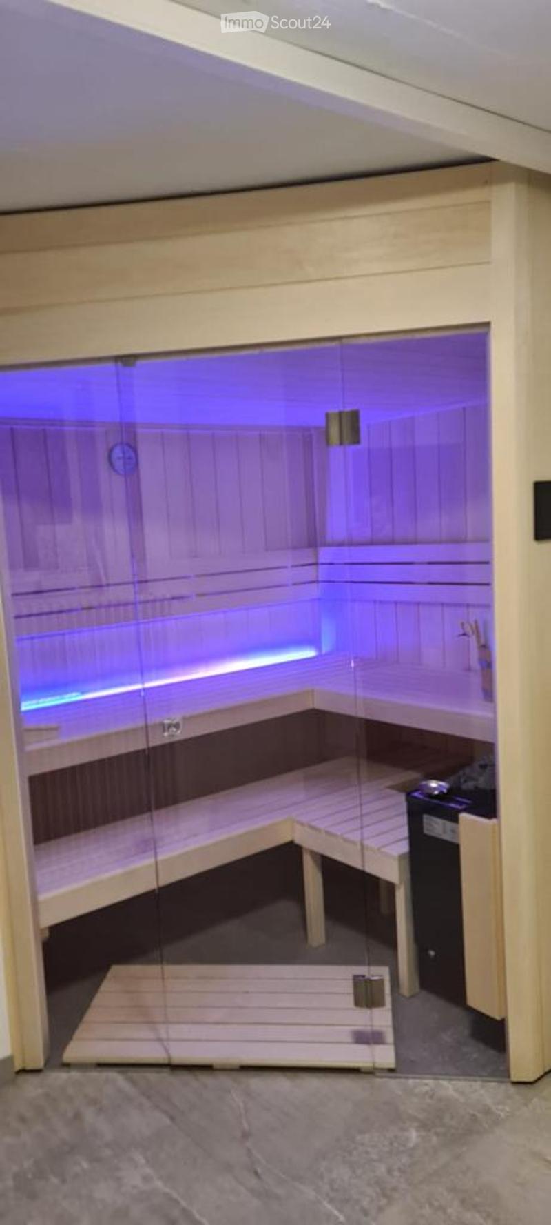 Modern sauna room with wooden benches, glass door, and purple lighting inside. Includes a control panel and a small step leading into the sauna.