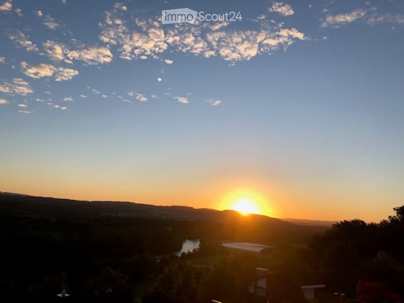 Scenic view of a sunset over a valley with a river and distant hills, with a small structure visible in the foreground.