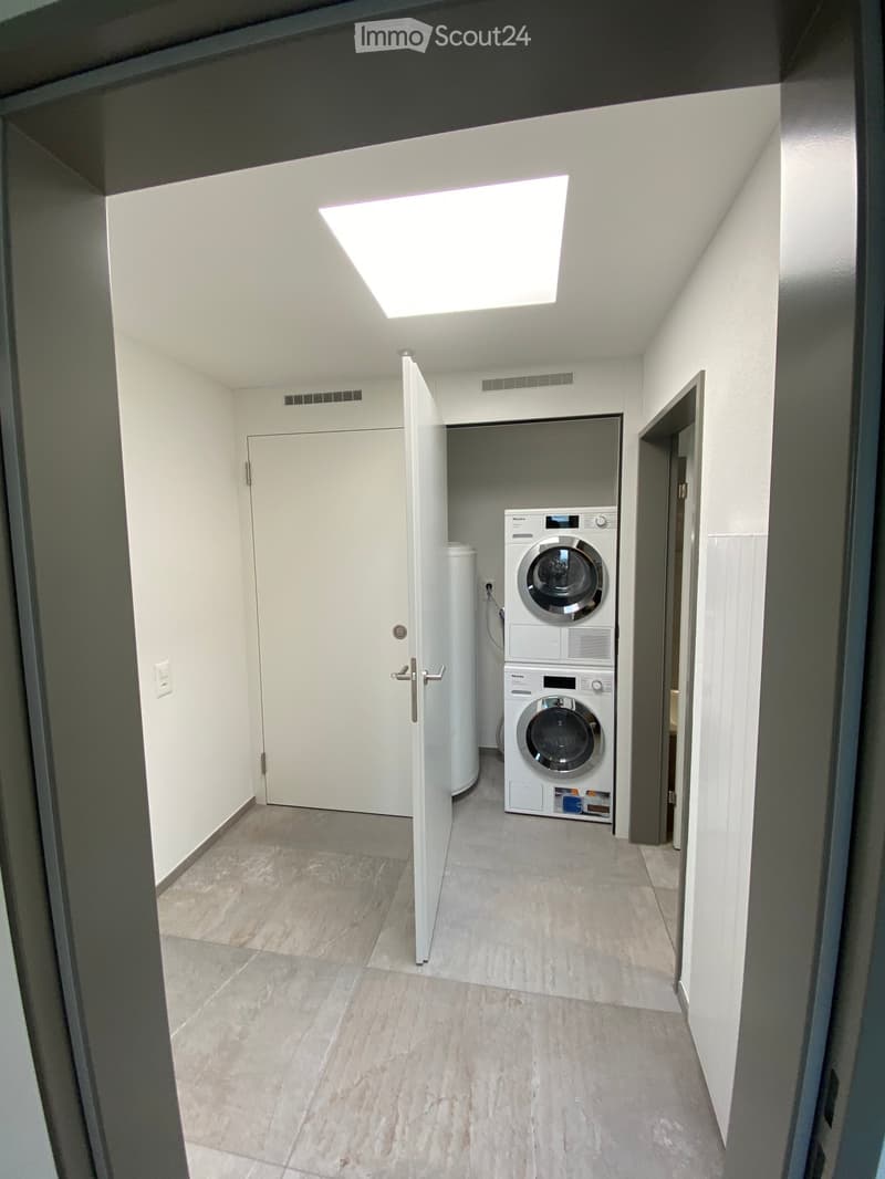 Clean, modern hallway with tiled floor, white walls, and a private washing machine in an adjacent room.