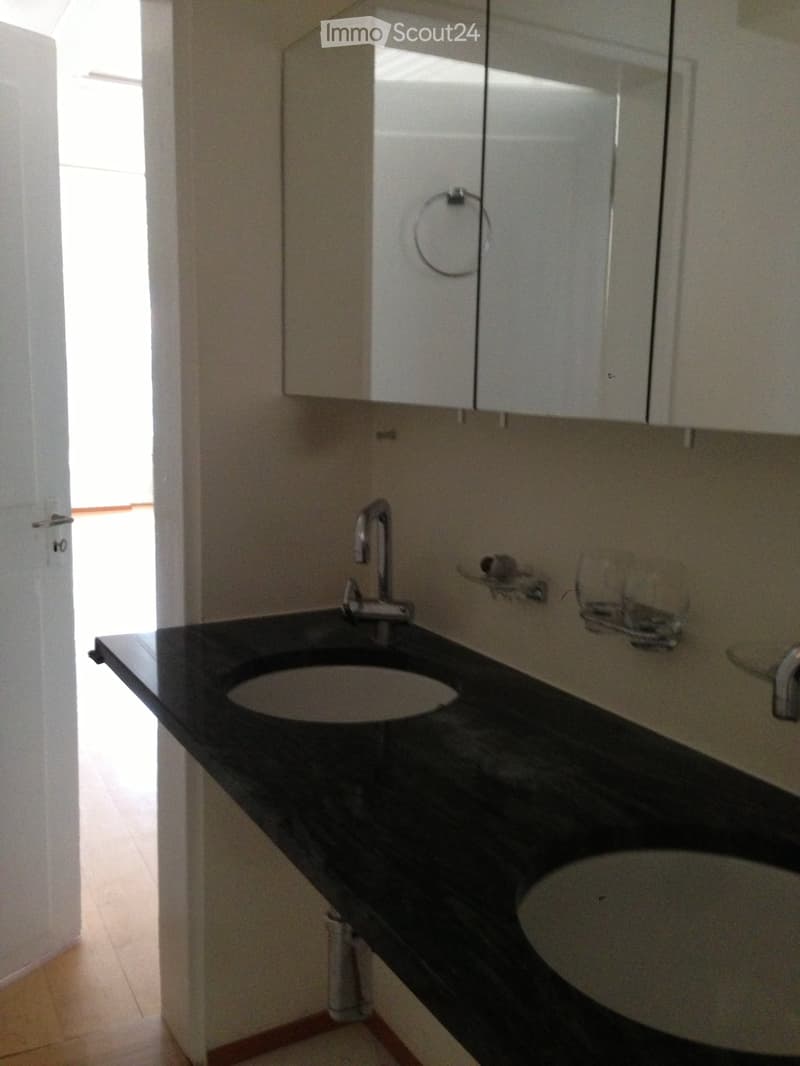 Modern bathroom with a black countertop, two sinks, a mirror, and white cabinets.