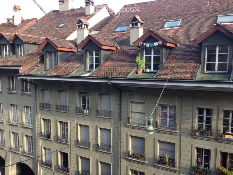 Multi-story residential building with red-tiled roof, multiple chimneys, dormer windows, and several balconies adorned with potted plants.
