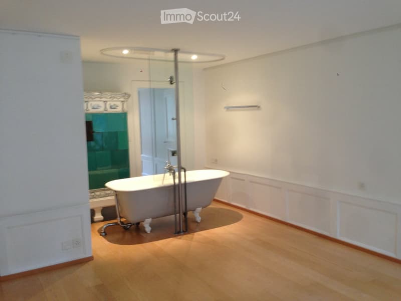 Bathroom with a freestanding bathtub, glass shower enclosure, and a decorative mirror. Light wooden flooring and white walls.