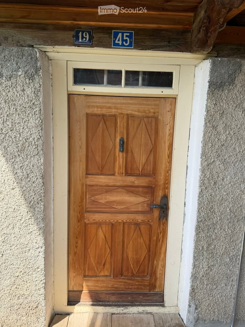 Wooden double door with decorative diamond patterns, small window above, and house numbers 19 and 45 displayed above the door.