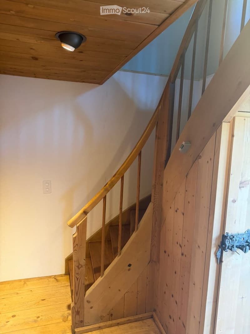 Wooden staircase with a handrail, wooden floor, and a wooden door with a metal handle.