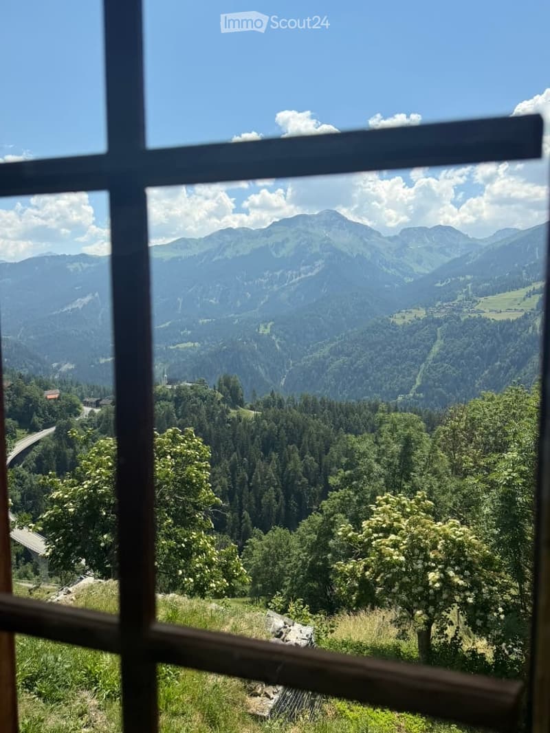 Panoramic mountain view from a balcony or terrace, with clear blue skies and lush green valleys.