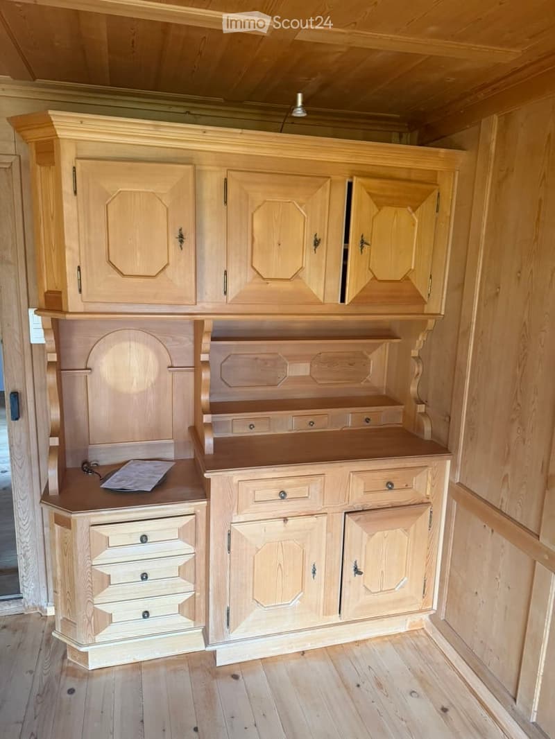 A well-furnished room with light wooden cabinets, a wooden desk, and multiple drawers, all set against a wooden-paneled wall and floor.