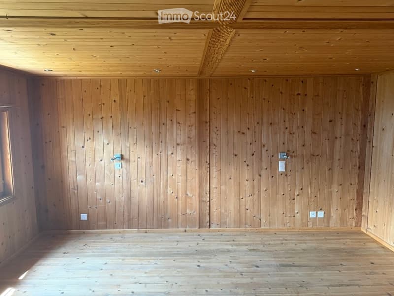 Empty room with wooden walls and ceiling, wooden floor, and a small window on one side.