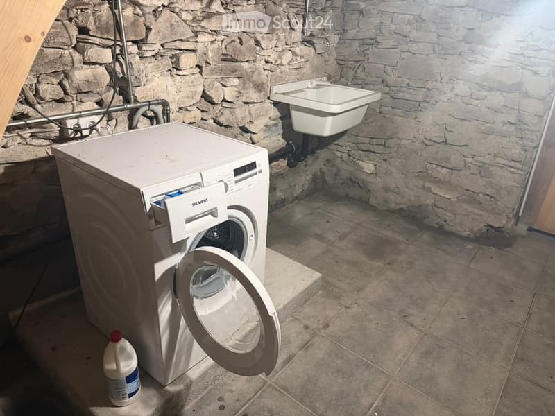 Bathroom with stone walls, tiled floor, white washing machine, and a small sink.