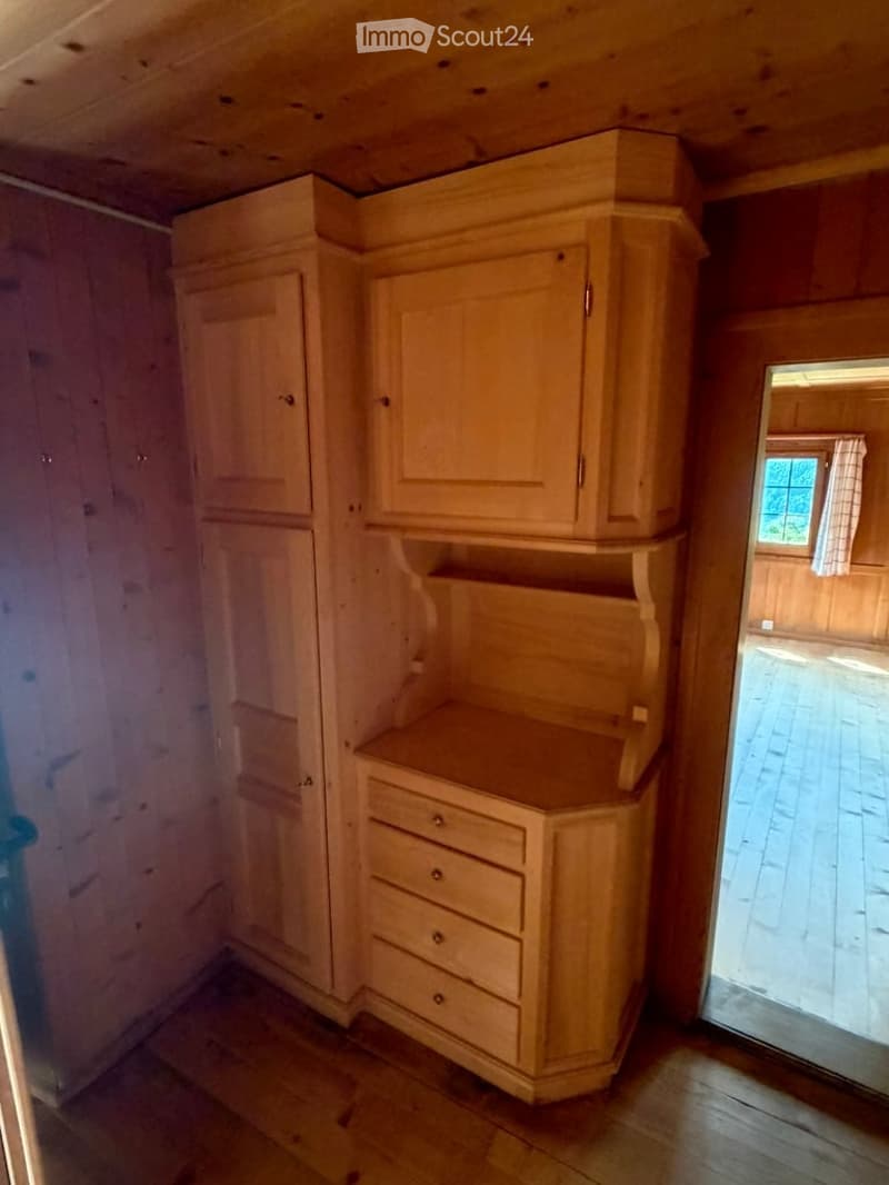 Corner kitchen with light wood cabinets and drawers, wooden countertop, and a small window in the background.