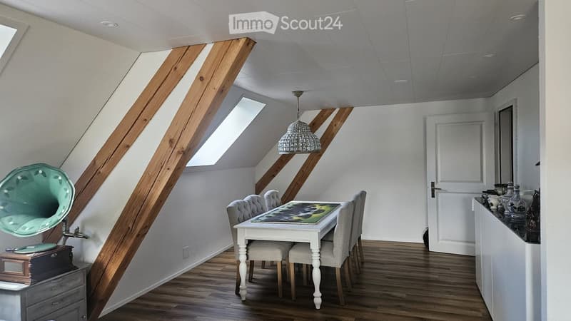 Bright attic room with wooden beams, skylights, and modern decor including a white dining table, chairs, gramophone, and decorative vases.