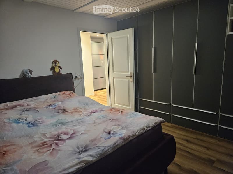Bedroom with a large bed, floral duvet, dark wooden wardrobe, and two stuffed toys on the headboard.