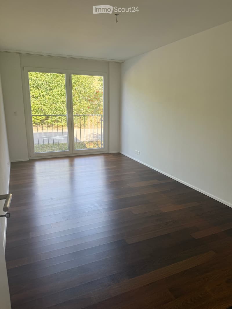 Empty room with wooden flooring, white walls, and large sliding glass doors leading to a balcony.